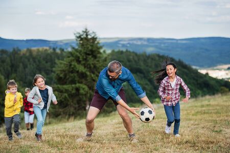 Group of school children with teacher on field trip in nature, playing with a ball.の写真素材