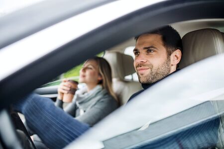 Happy young couple with coffee sitting in car, driving.