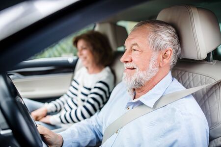 Happy senior couple with smartphone sitting in car, driving,.