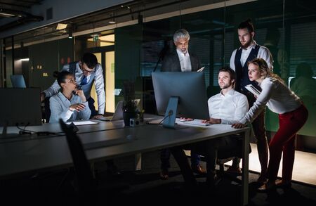 A group of business people in an office at night, using computer.
