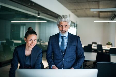 Two businesspeople with computer standing in an office at desk.の写真素材