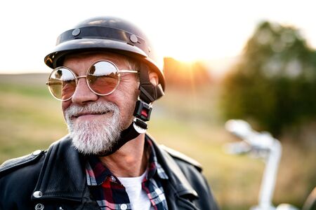 A cheerful senior man traveller with motorbike in countryside, headshot.の写真素材