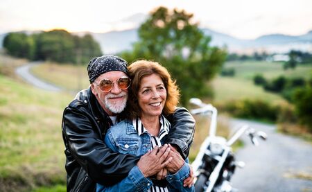 A cheerful senior couple travellers with motorbike in countryside.の写真素材