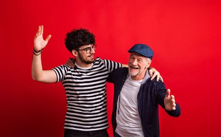 Young man and senior father in a studio on red background.