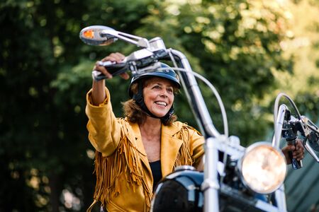 Cheerful senior woman traveller with motorbike in town.の写真素材