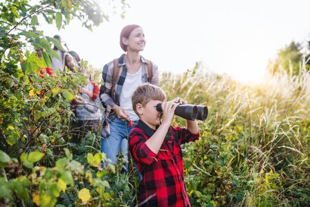 Group of school children with teacher on field trip in nature, using binoculars.