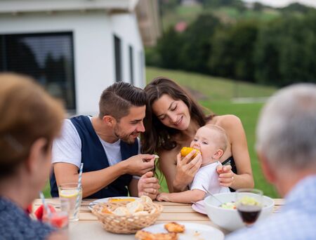 Portrait of multigeneration family sitting at table outdoors on garden barbecue.
