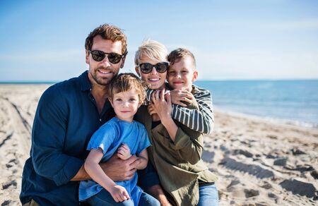 Young family with two small children sitting outdoors on beach.