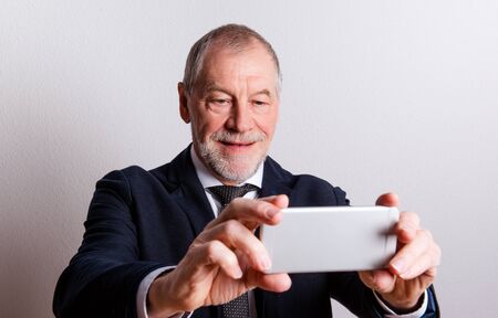 Portrait of a senior man with smartphone in a studio, taking selfie.の写真素材
