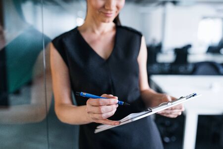 Midsection of young businesswoman with clipboard in an office, standing.
