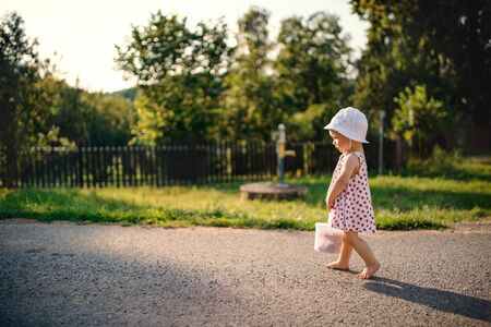 A cute toddler girl walking outdoors on road in countryside in summer.の写真素材