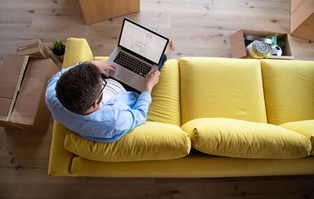 Top view of mature man sitting on sofa in unfurnished house, using laptop. A moving in new home concept.の写真素材