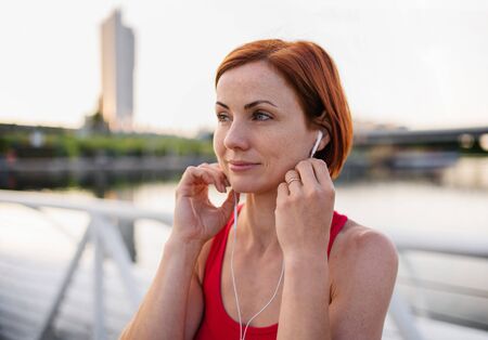 Front view of young woman runner with earphones in city, resting.の写真素材