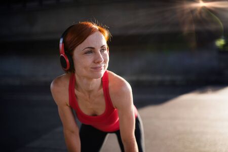 Young woman with headphones resting after doing exercise outdoors in city.の写真素材