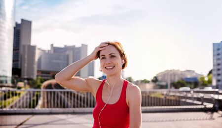 Front view of young woman runner with earphones in city, resting.の写真素材