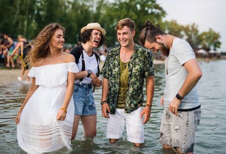 Group of young friends at summer festival, standing in lake.