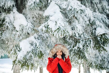 A front view portrait of young woman standing outdoors in snowy winter forest.