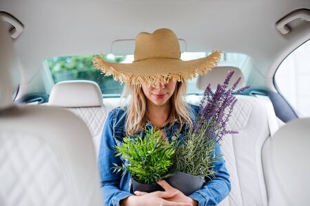 Young woman with hat and plants sitting in car, having fun.