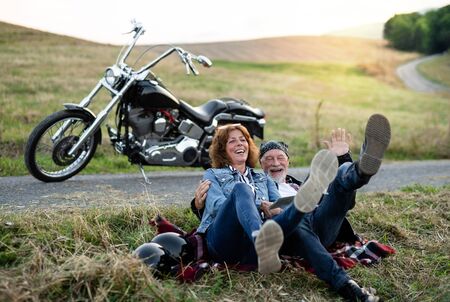 A cheerful senior couple travellers with motorbike in countryside.の写真素材