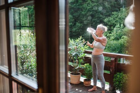 A senior woman with sports bra outdoors on a terrace in summer, drinking water.の写真素材