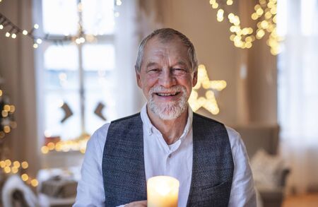 Front view of happy senior man indoors holding candle at Christmas.