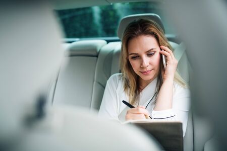Business woman with smartphone sitting on back seats in taxi car.の写真素材