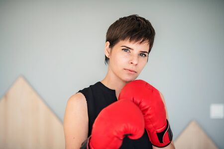 Front view of young woman with boxing gloves standing indoors at home.の写真素材