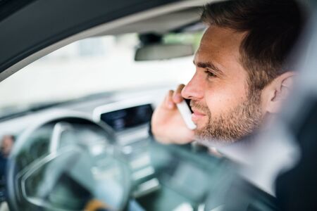 Young businessman with smartphone sitting in car, making phone call.の写真素材