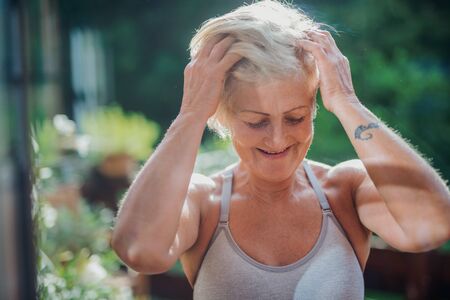 A senior woman with sports bra standing outdoors on a terrace in summer.の写真素材