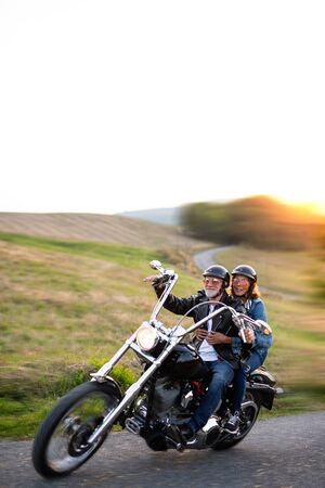 A cheerful senior couple travellers with motorbike in countryside.