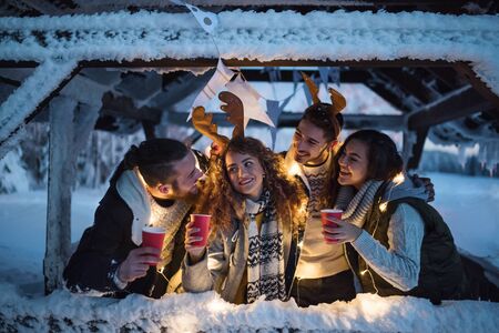Group of young friends outdoors in snow in winter at night, holding drinks.の写真素材