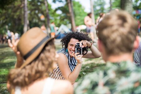 Group of young friends sitting on ground at summer festival, taking photo.の写真素材