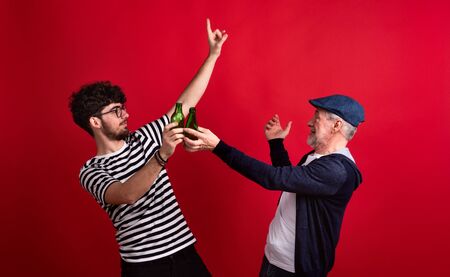 Young man and senior father with bottles in a studio on red background.の写真素材