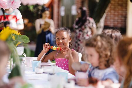 Small children sitting at the table outdoors on garden party, eating.の写真素材