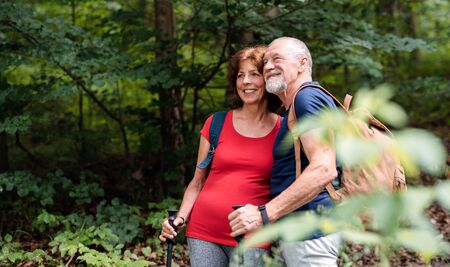 Senior tourist couple with backpacks on a walk in forest in nature.
