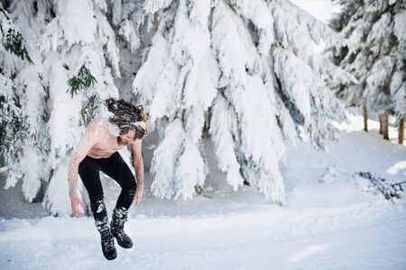 Topless young man outdoors in snow in winter forest, having fun.