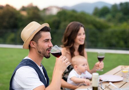 Young couple with baby sitting at table outdoors on family garden barbecue.の写真素材