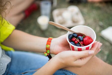 Unrecognizable woman at summer festival, sitting on the ground and eating fruit.の写真素材