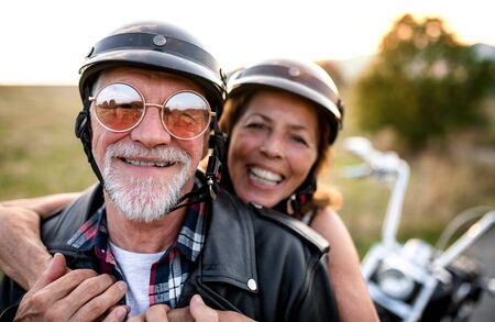 A cheerful senior couple travellers with motorbike in countryside.の写真素材
