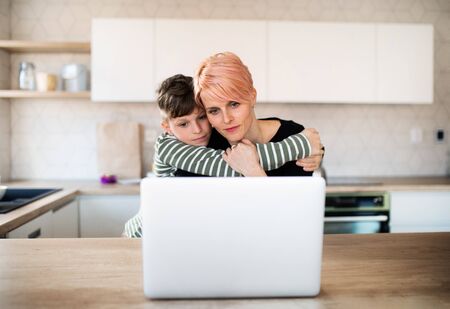 A young woman with a small son using laptop in a kitchen at home.の写真素材