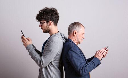 Portrait of a senior father and young son in a studio, using smartphones.の写真素材