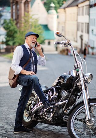 A senior businessman with motorbike in town, using smartphone.の写真素材