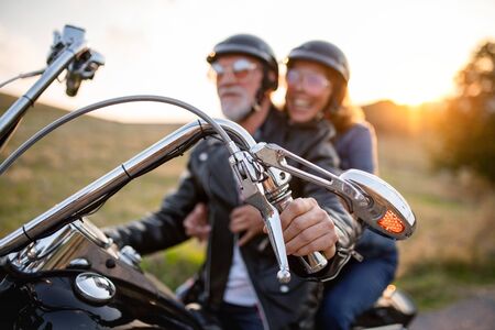 A cheerful senior couple travellers with motorbike in countryside at sunset.の写真素材