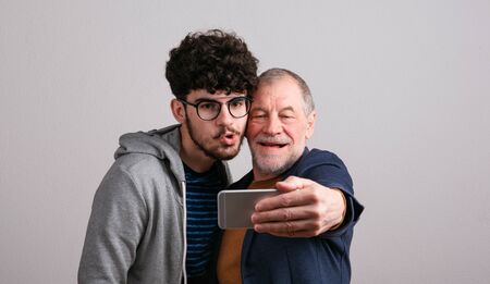 Portrait of a senior father and young son in a studio, taking selfie.