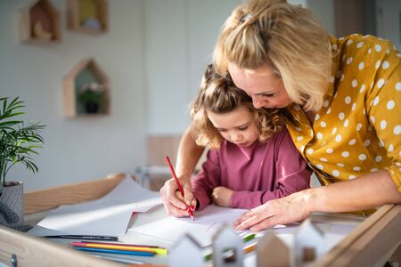 A cute small girl with mother indoors at home, drawing pictures.の写真素材
