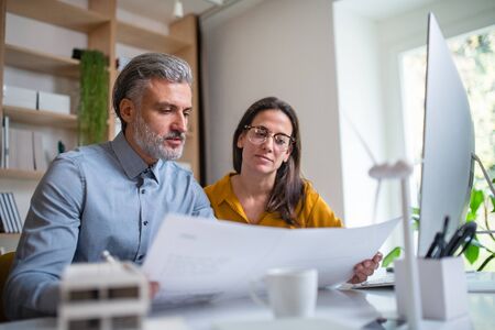 Architects sitting at the desk indoors in office, looking at blueprints.