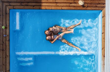 Top view of father with small children sitting in swimming pool outdoors.の写真素材