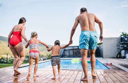 Rear view of family with two small children by swimming pool outdoors.の写真素材