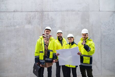 A group of engineers standing against concrete wall on construction site.