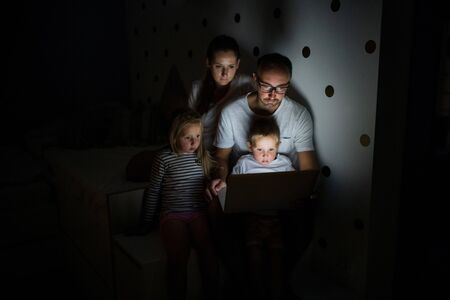 Family with children sitting indoors in bedroom, using laptop.の写真素材